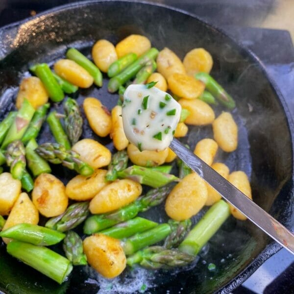 pat of herb butter over gnocchi and asparagus in cast iron fry pan