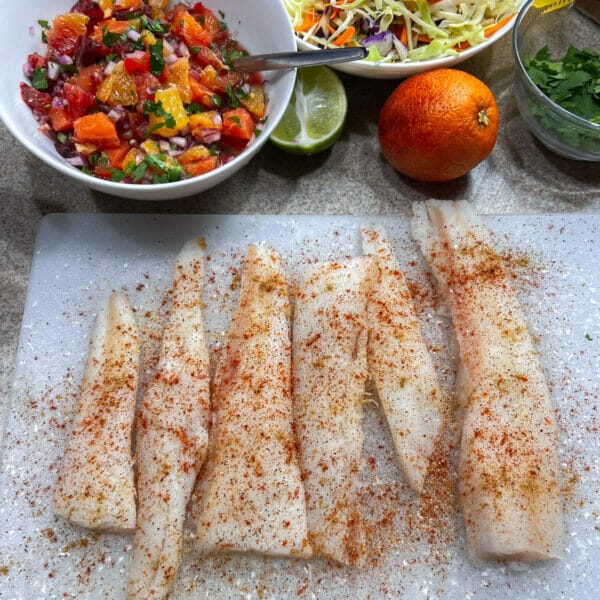 well seasoned white fish on cutting board with orange fruit salsa in back
