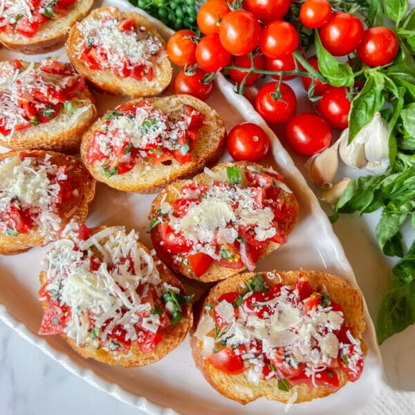 tomato bruschetta toasts on white platter with cherry tomatoes on side