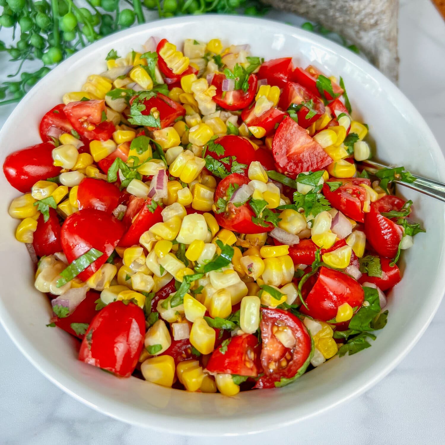 white bowl filled with corn salad, close up. corn, tomatoes, cilantro, red onion.