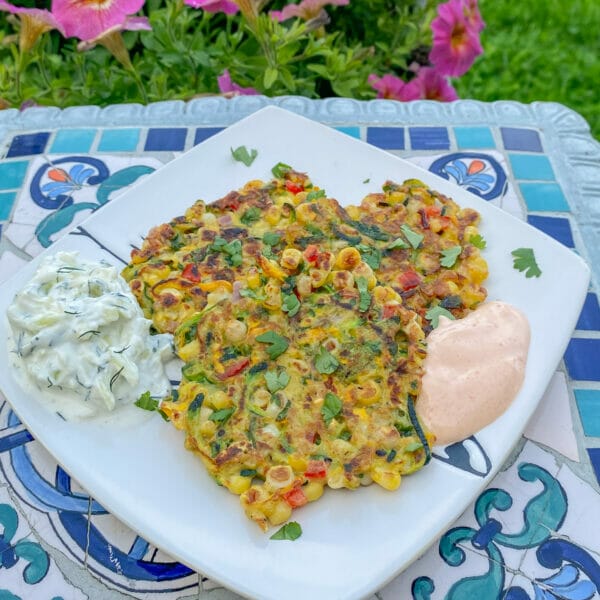 zucchini corn fritters on plate outside with two dipping sauces 