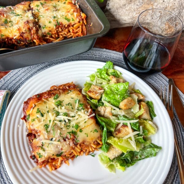 baked spaghetti on plate with caesar salad glass of wine