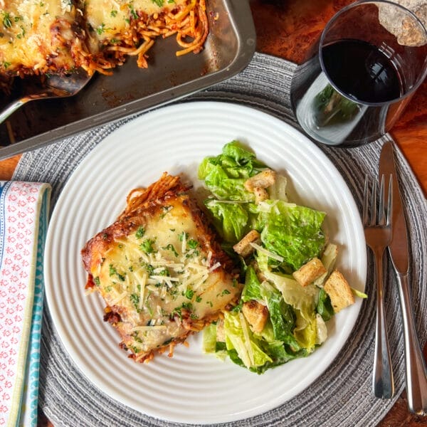 top down view of baked spaghetti on plate with salad, cutlery and wine