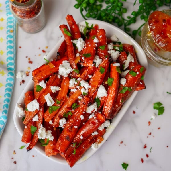 roasted carrot spears with cheese and parsley on white serving plate