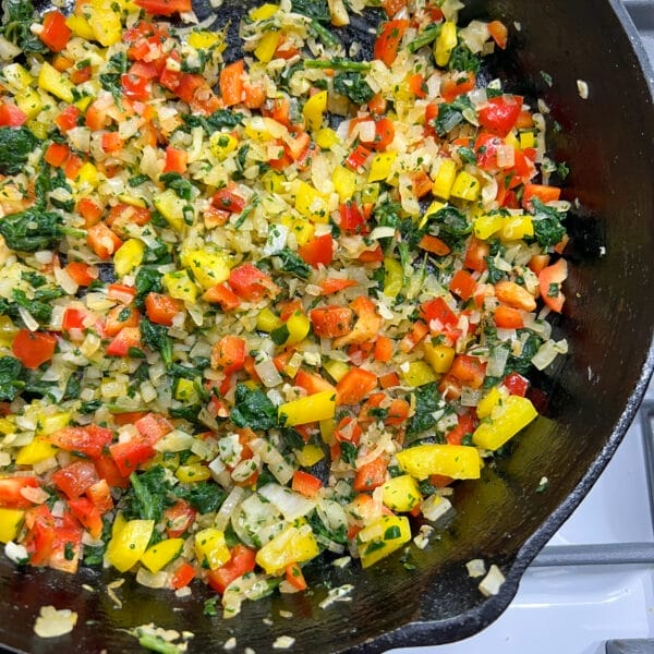 diced colorful peppers, spinach and onions in cast iron fry pan