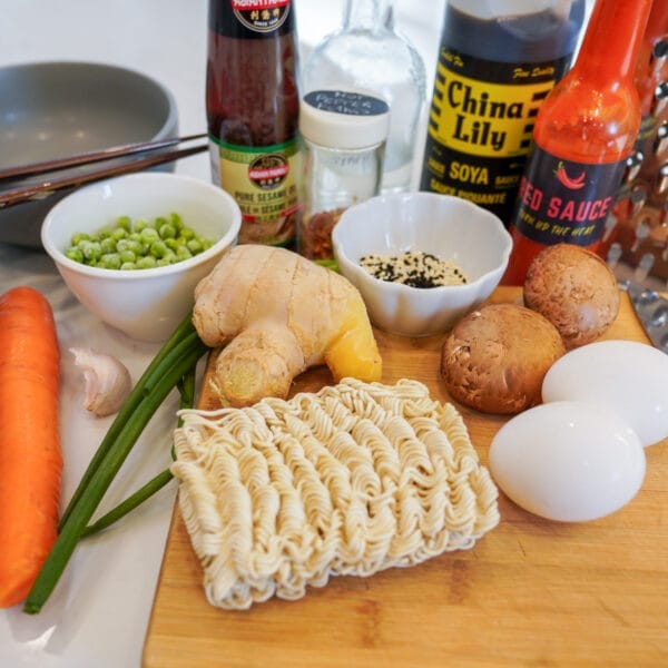 aromatics, mushroom, carrots, seasoning, eggs and ramen noodles on cutting board ready to make soup