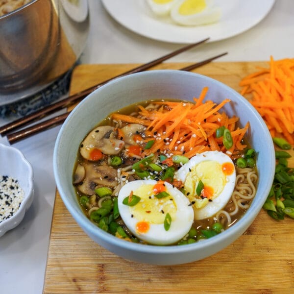 bowl of ramen soup with carrots, mushrooms, eggs on counter with chop sticks