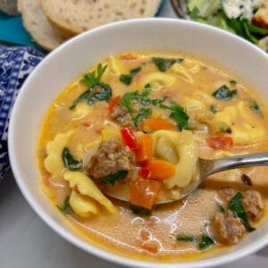 close up of spoon full of sausage, tortellini and veggies in creamy broth