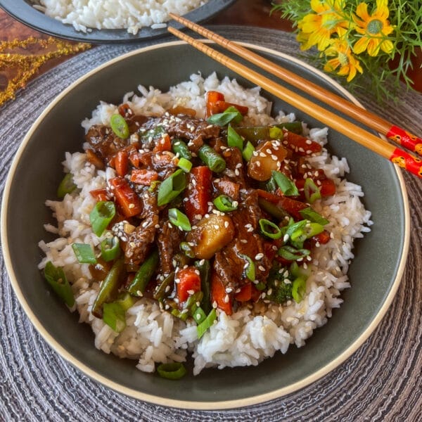 saucy beef and vegetable stir fry on rice in bowl chopsticks