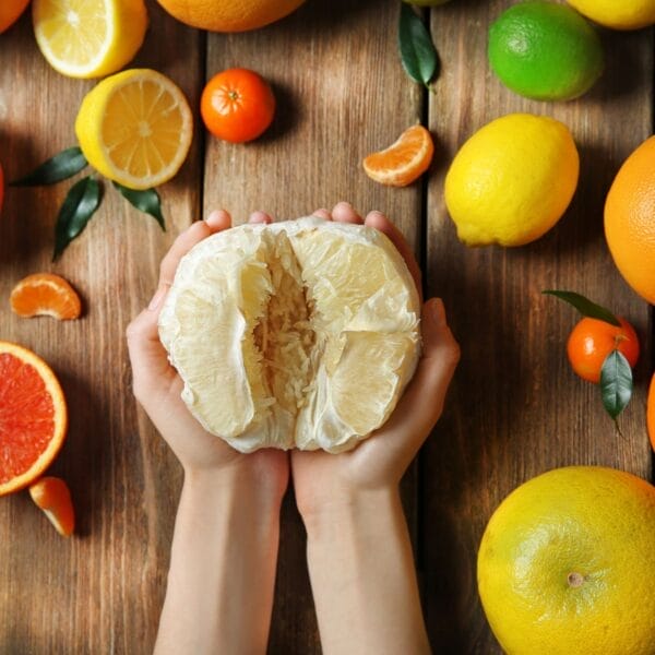 hand holding a pomelo without the peel on wood board with other citrus fruit
