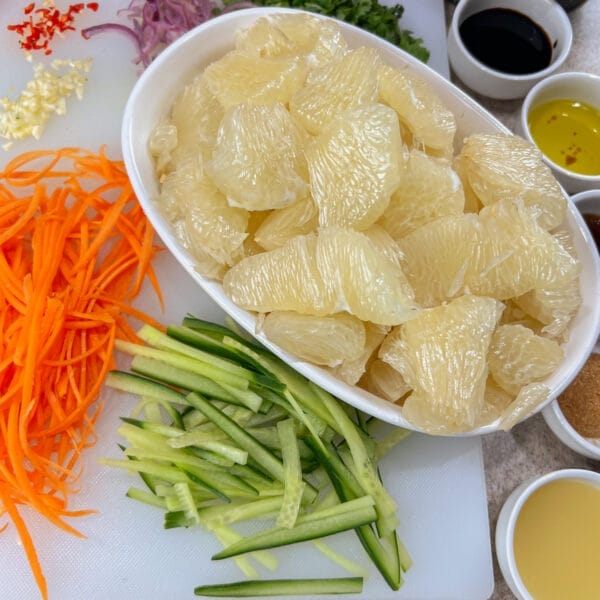 ingredients on cutting board for pomelo salad showing pomelo, cucumbers, carrots and dressing ingredients