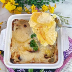 cooked scalloped potatoes on spoon over casserole dish
