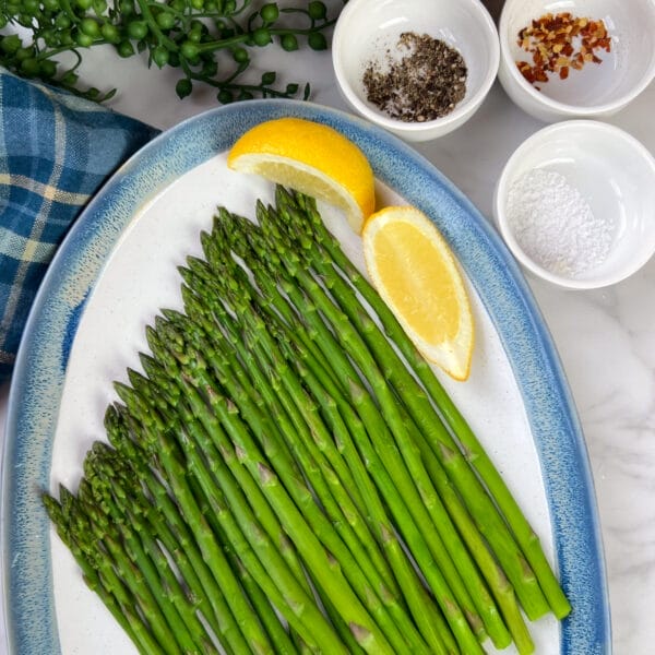 steamed asparagus on platter with lemon wedges and seasonings