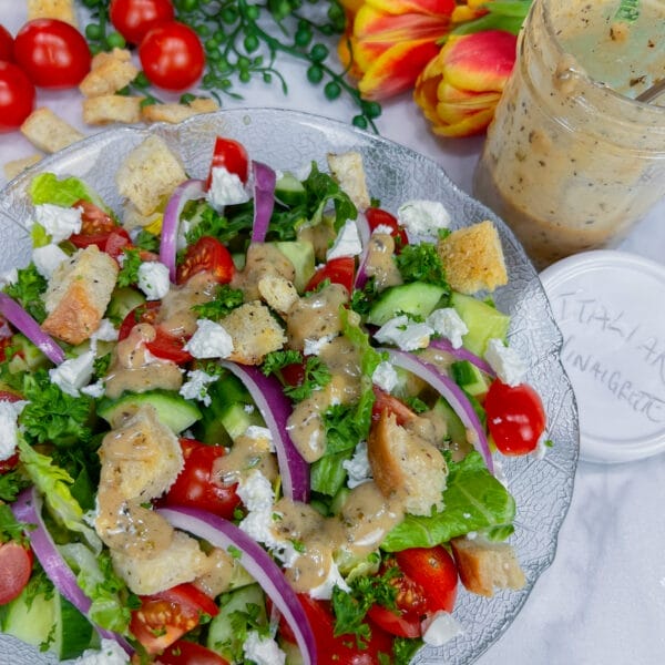 colorful salad on plate with Italian dressing in jar on side