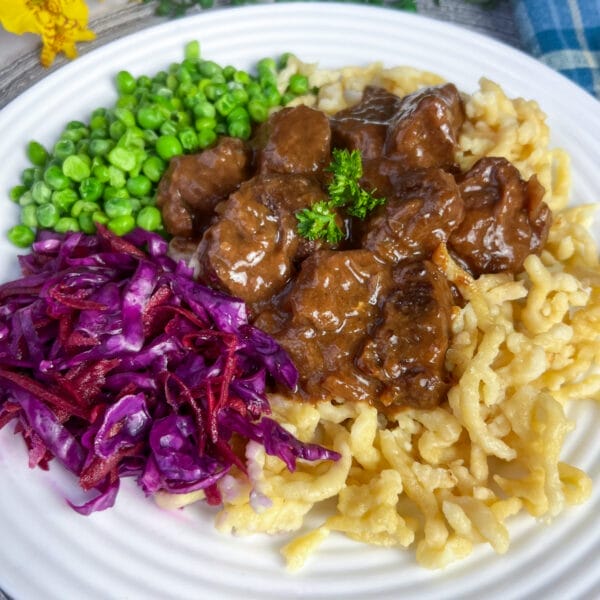 goulash on noodles on plate with veggie sides